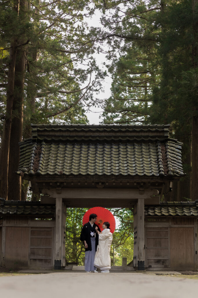 立山寺の門前で番傘を持って見つめ合う和装新郎新婦