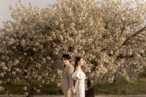 富山県の桜のロケーションで撮影されたフォトウェディング。満開の桜の下、洋装の新郎新婦が手をつないで立つ美しい写真。