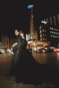 富山の夜の街並みでフォトウェディングを行う黒ドレスと黒スーツの新郎新婦の前撮り写真