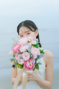 富山の海ロケーションフォトウェディングでピンクのブーケを持ってカメラ目線の洋装花嫁のソロ前撮り写真